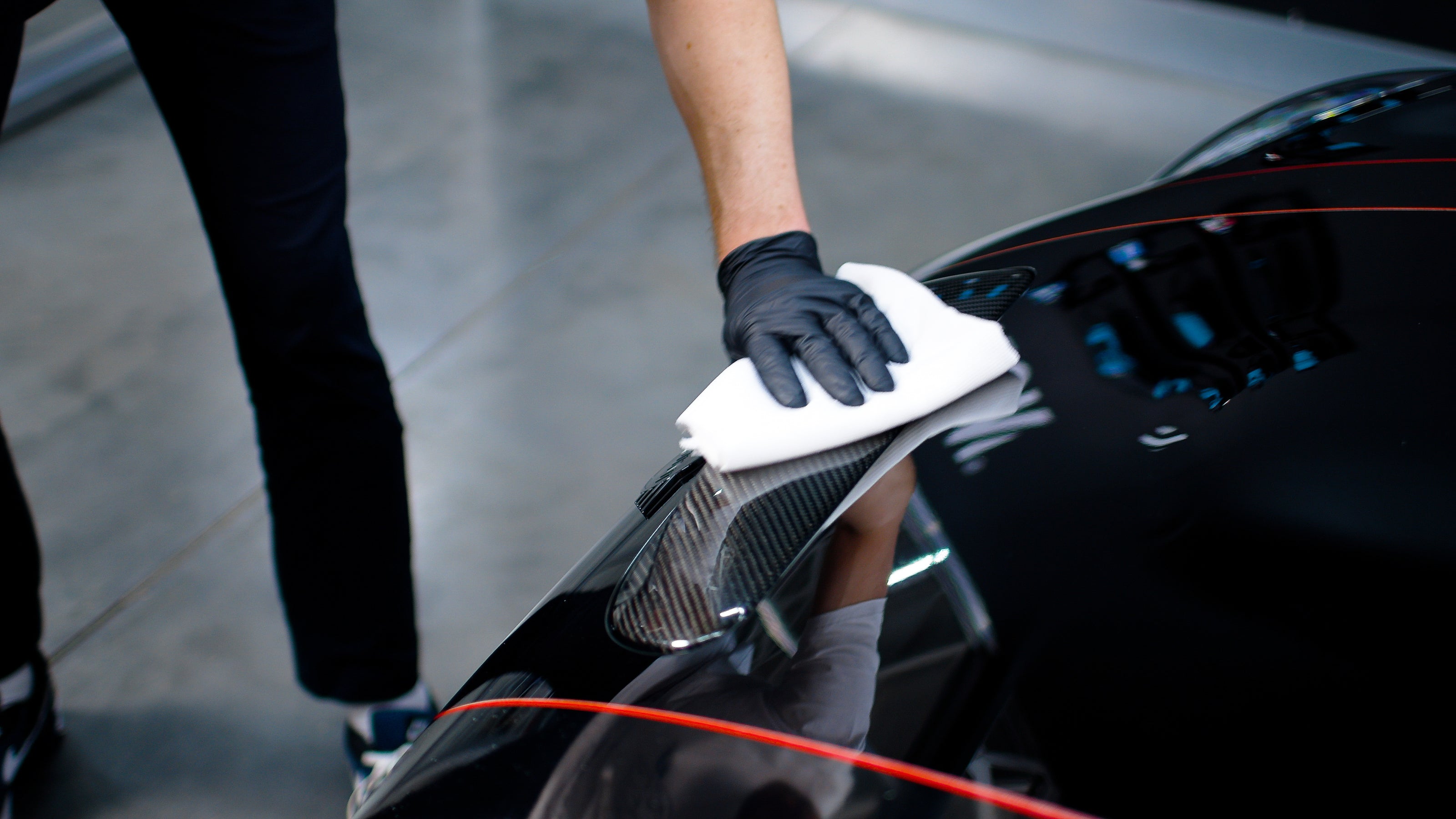 Hand in Handschuhen wischt Autokarosserie mit Mikrofasertuch