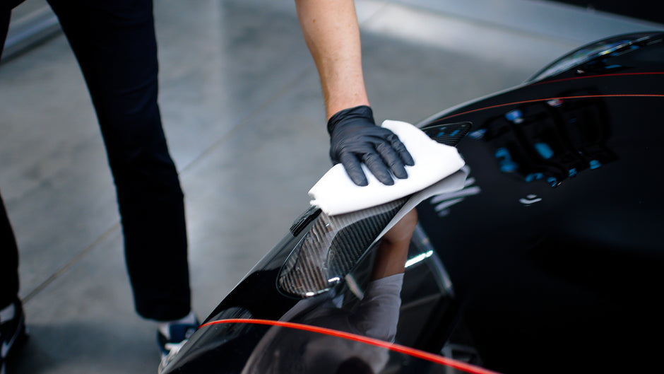 Hand in Handschuhen wischt Autokarosserie mit Mikrofasertuch