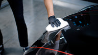 Hand in Handschuhen wischt Autokarosserie mit Mikrofasertuch