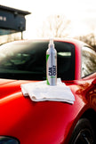 Kleinsprühflasche und Mikrofasertuch auf roter Autokarosserie